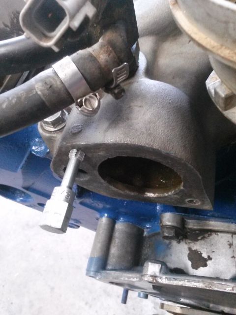 1996 Ford Bronco - A close-up shot shows a metal engine component with a hose clamp and a socket wrench attached to a bolt. The engine part is painted blue in…