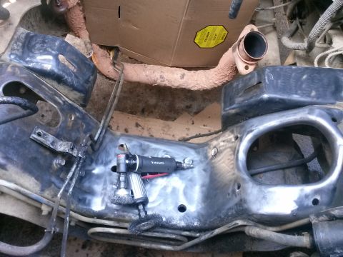 1996 Ford Bronco - A close-up view of a vehicle's metal frame being worked on with a pneumatic grinder. A rusty exhaust pipe is visible in the background.