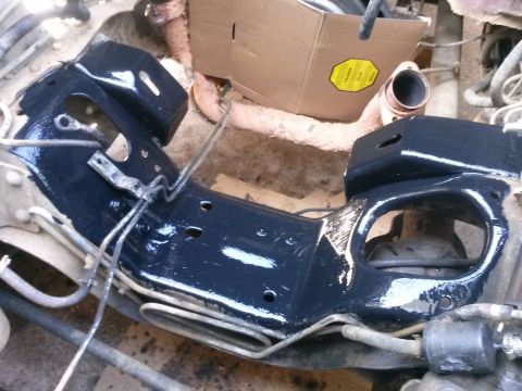 1996 Ford Bronco - A close-up view of a black-painted frame component of a vehicle, likely a truck or SUV, with various metal lines and brackets attached. The…