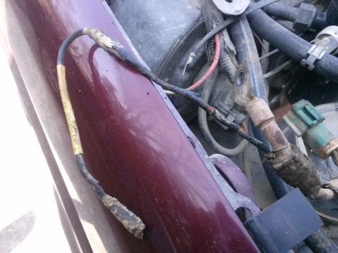 1996 Ford Bronco - A close-up view of damaged wiring harness connected to a vehicle's engine bay. The harness is black with yellow tape and shows signs of fra…