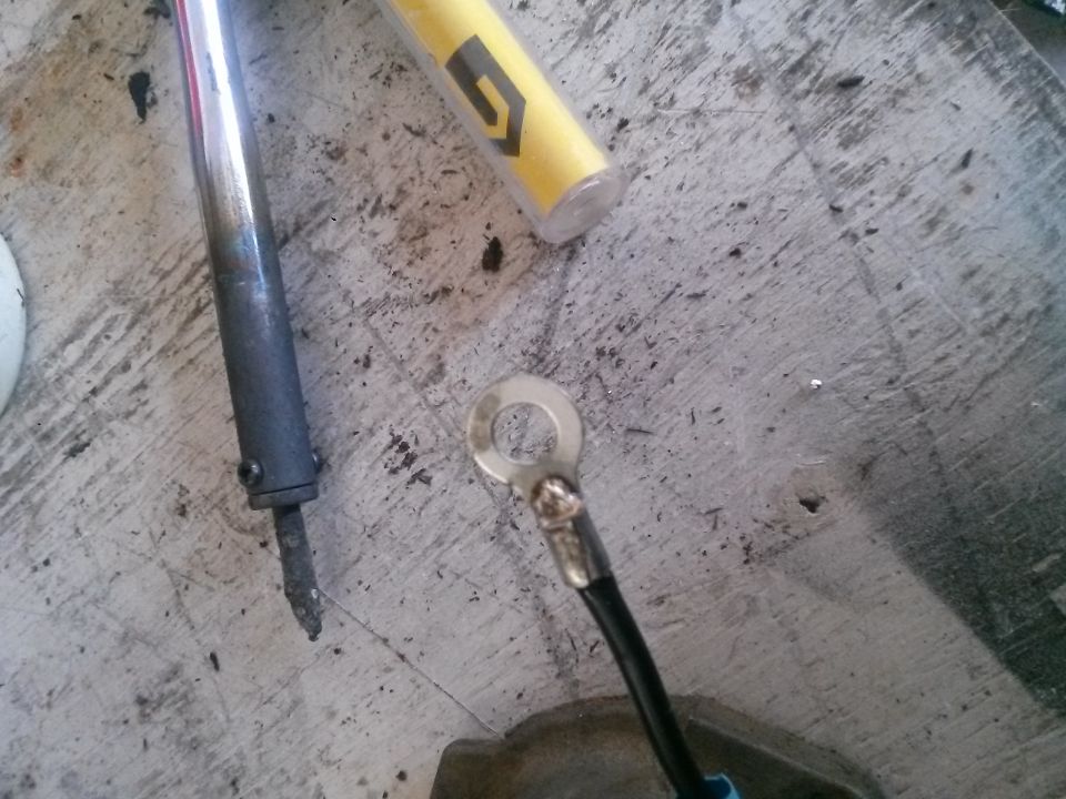 Soldering iron and a ring terminal with a black wire on a concrete surface.
