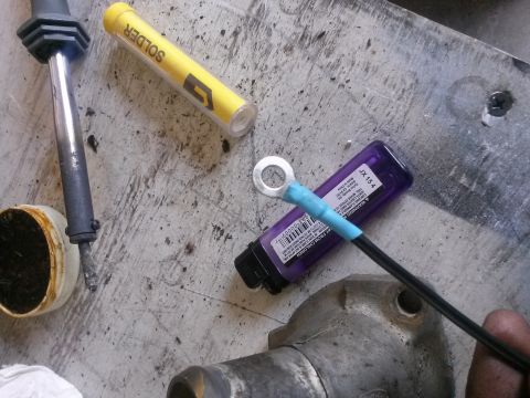 1996 Ford Bronco - A close-up view of electrical wiring components including a soldering iron, solder, heat shrink tubing, and a ring terminal, laid out on a…