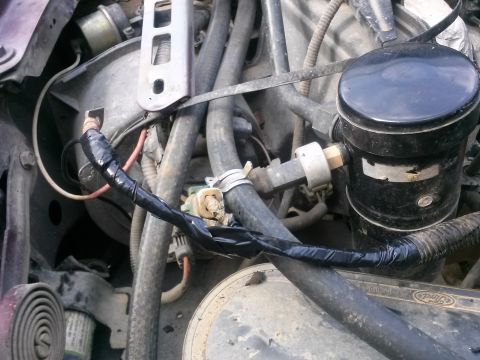 1996 Ford Bronco - A close-up view of a section of an engine bay, focusing on wiring that has been wrapped in black electrical tape. A black cylindrical compo…