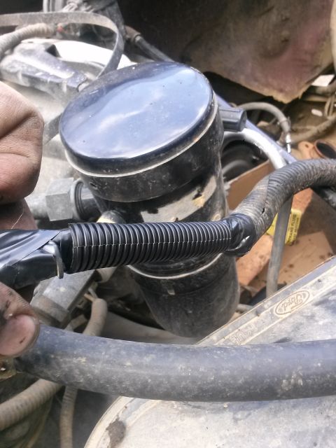 1996 Ford Bronco - A close-up view of a black corrugated hose secured with black electrical tape to a larger black component in an engine bay. The hose appear…