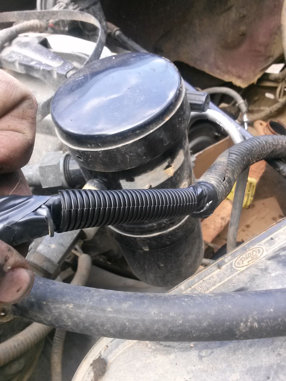 Close-up of a black corrugated hose with electrical tape in a vehicle engine bay.