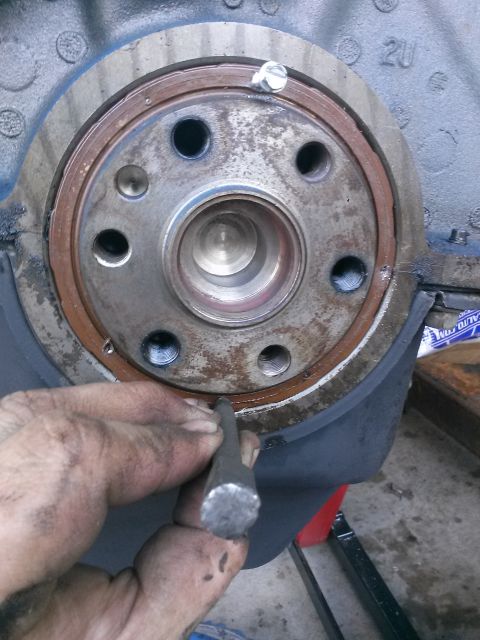 1996 Ford Bronco - A mechanic's dirty hands use a chisel to pry a rusty seal from a metal engine component. The component has several bolt holes and a central…