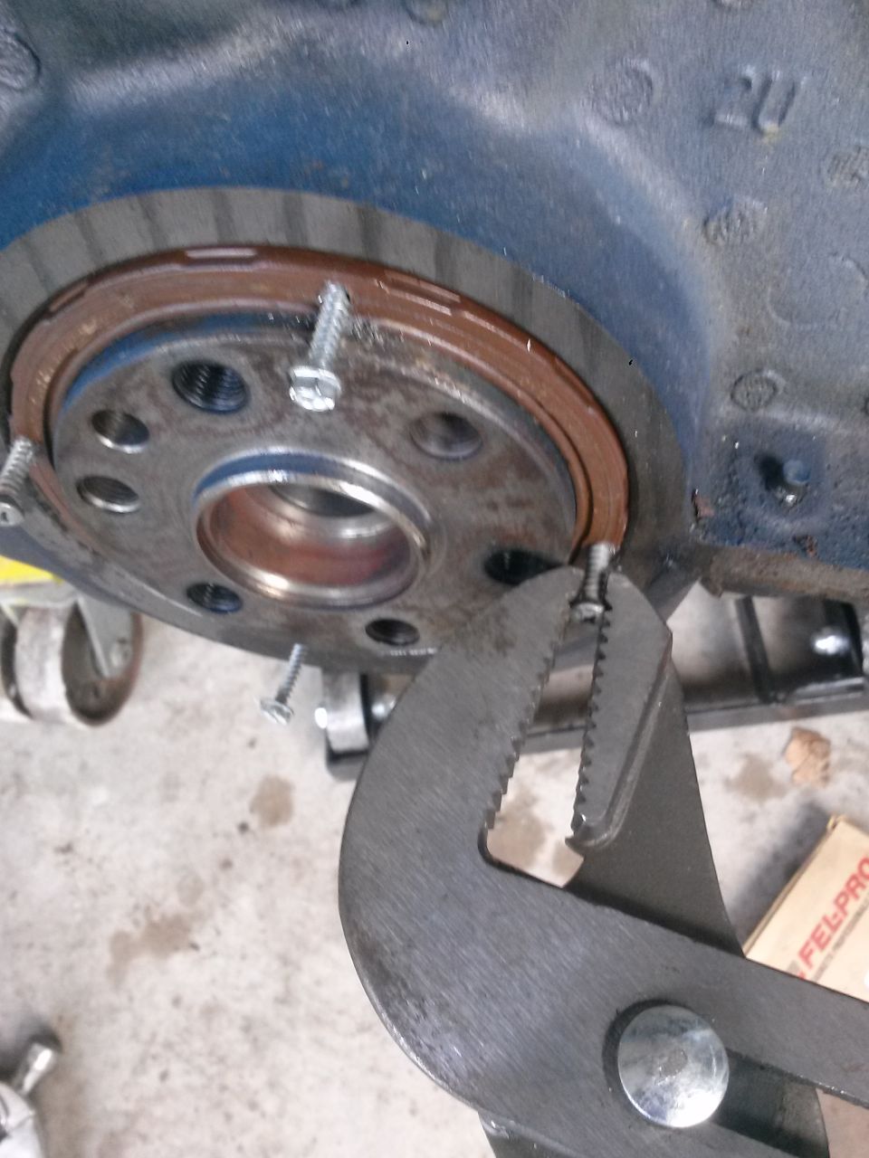 Close-up of pliers gripping a screw on a blue engine block near a rusty seal.