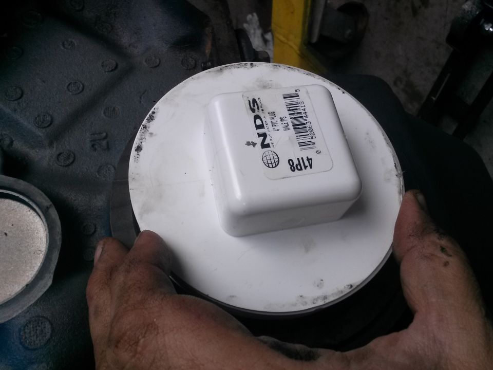 Hands holding a white NDS 4" PVC plug over a white circular object on a dark textured surface.