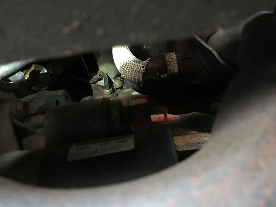 Close-up of a vehicle starter motor with wiring and exhaust components.