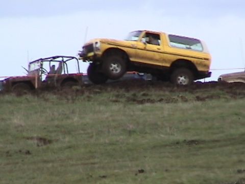 1994 Ford Explorer - Yellow Ford Bronco being towed by a red Jeep in muddy off-road conditions.