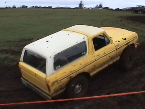 1994 Ford Explorer - A yellow Ford Bronco navigates a muddy terrain, with several other vehicles in the distance.