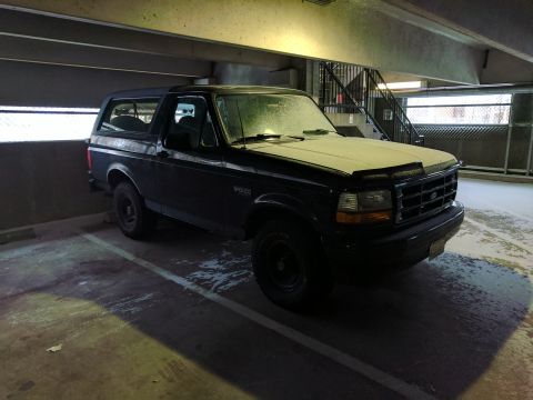 1995 Ford Bronco - A dark-colored Ford Bronco is parked in a covered parking garage with a light dusting of snow on its hood and windshield. The vehicle is vi…