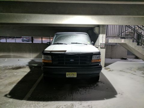 1995 Ford Bronco - A black Ford Bronco is parked in a concrete parking garage with snow on the ground and on the vehicle. The front of the SUV is visible, sho…