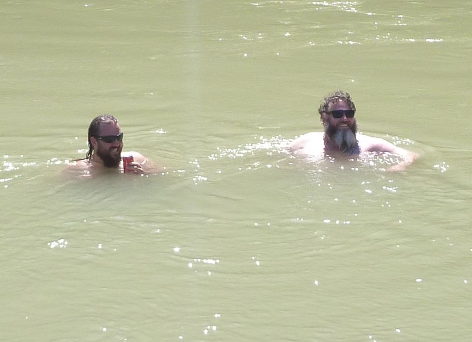 Two men swimming in water, one holding a red can.