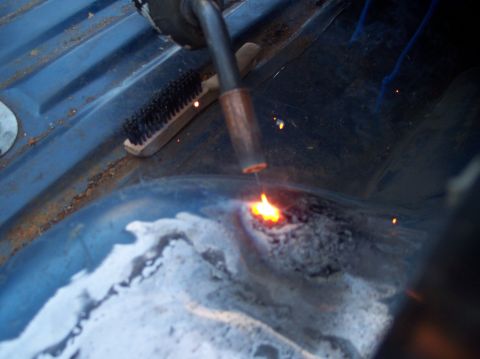 1990 Ford Bronco - Welding a rusted section of a vehicle's floor pan with a wire brush visible.