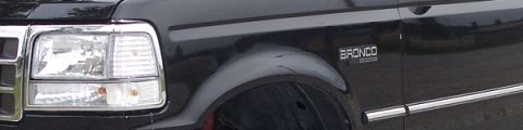 1989 Ford Bronco - A close-up view of the front fender and headlight area of a black Ford Bronco. The vehicle has chrome trim around the headlight and a "BRON…