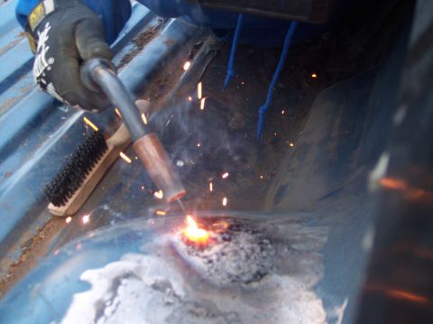 1990 Ford Bronco - A person is welding a rusty section of a vehicle's floor pan, with sparks flying from the weld.
