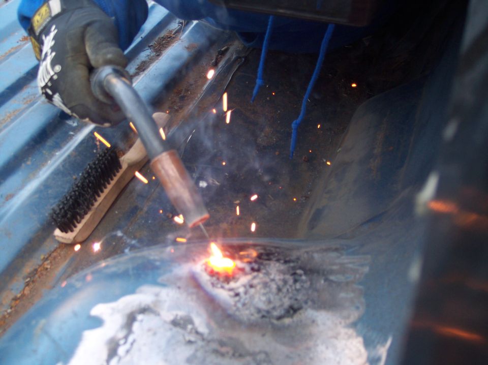 welder working on rusty floor pan, sparks flying