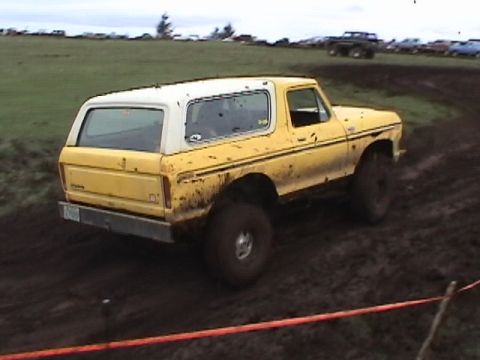 1994 Ford Explorer - Muddy yellow and white SUV navigates a dirt track with other vehicles in the background.