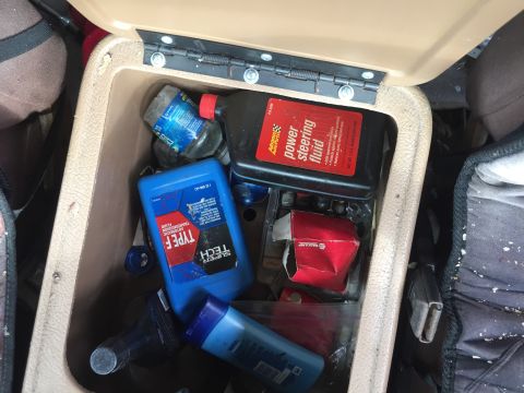 1979 Ford Bronco - Vehicle interior storage compartment contains various automotive fluids and tools.