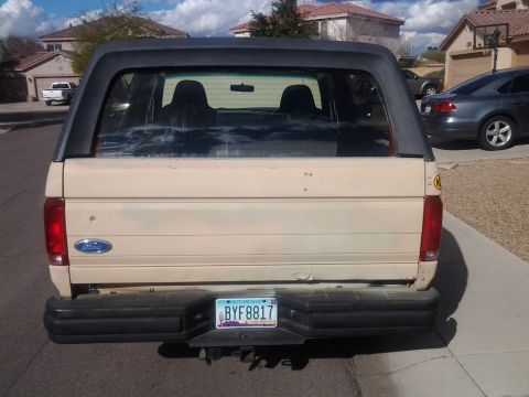 1991 Ford Bronco - Rear view of a tan Ford Bronco with a black bumper and tinted windows.