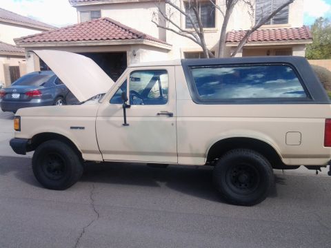 1991 Ford Bronco - A tan 1991 Ford Bronco is parked in front of a house with its hood open.