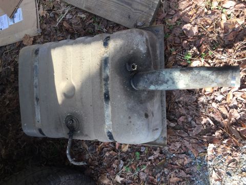 1979 Ford Bronco - A used fuel tank is shown lying on the ground outdoors.