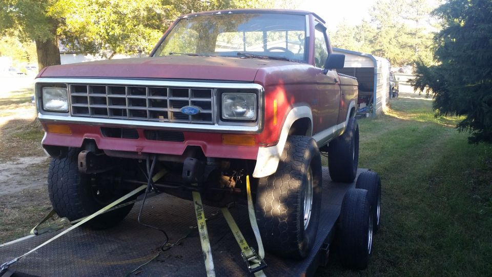 Lifted red Ford Ranger pickup with big tires strapped to a flatbed trailer, front bumper removed