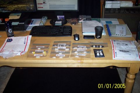 1995 Ford Bronco - A desk is covered with various small parts in labeled bags, mail, and office supplies.