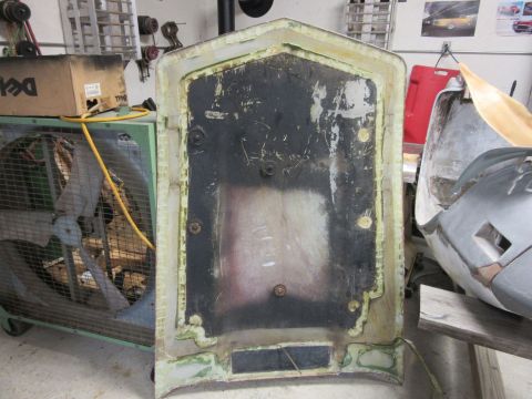 1976 Chevrolet Corvette - The underside of a car hood is shown, with a large industrial fan and other workshop items in the background.