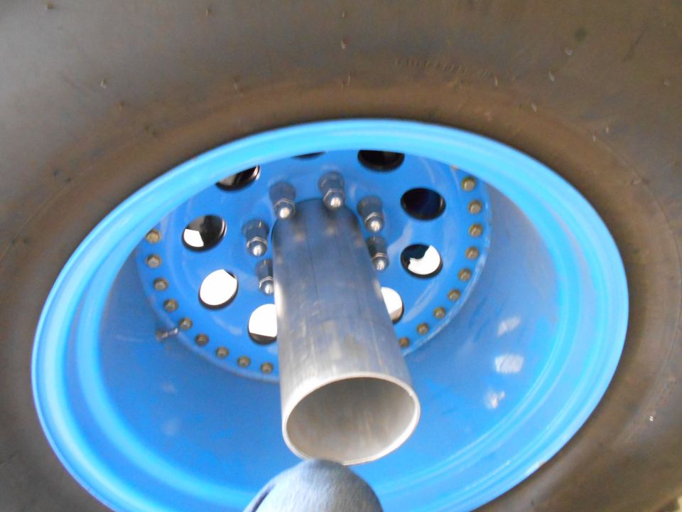 Close-up of a blue wheel with lug nuts and a metal pipe.