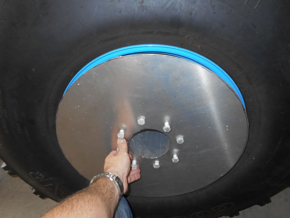 Close-up of a large tire with a metal plate and bolts, a blue ring is visible.