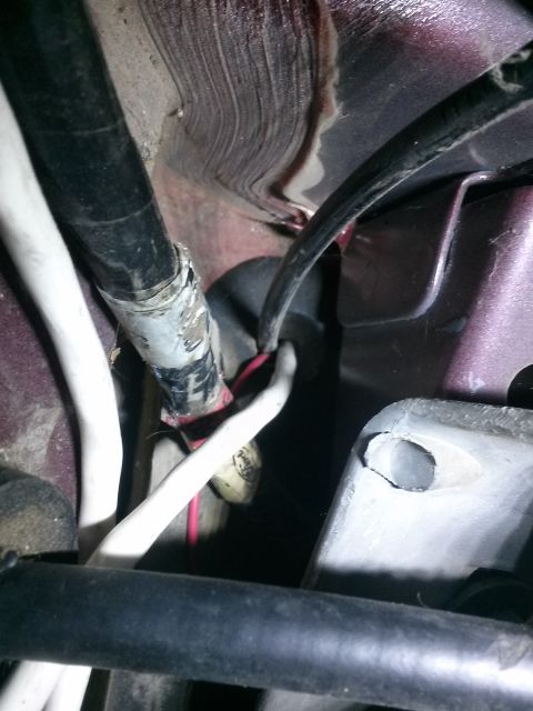 1996 Ford Bronco - Close-up view of wiring harness and metal bracket under the hood of a vehicle. Electrical tape is visible on a black wire bundle, with a re…