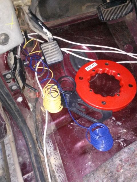 1996 Ford Bronco - A close-up view of the driver's side floorboard of a vehicle, showing various electrical wires and a red Cen-Tech wire spool.