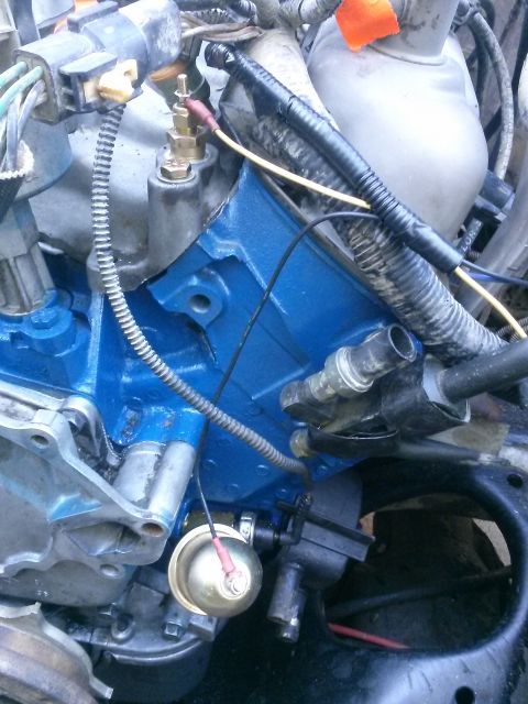 1996 Ford Bronco - A close-up view of a blue-painted engine block with various sensors and wiring attached. A brass temperature sensor with a red wire connect…