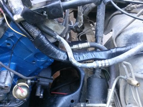 1996 Ford Bronco - A close-up view of the engine bay of a 1996 Ford Bronco, showing various hoses, wiring, and the blue-painted engine block.