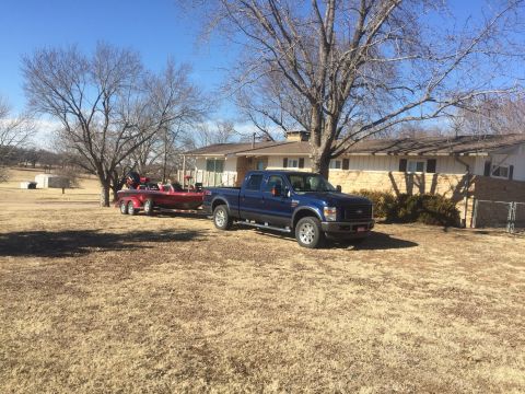 1982 Ford Bronco - A blue Ford F-Series truck is parked on dry grass next to a red boat on a trailer. A ranch-style house with a stone facade is visible in th…