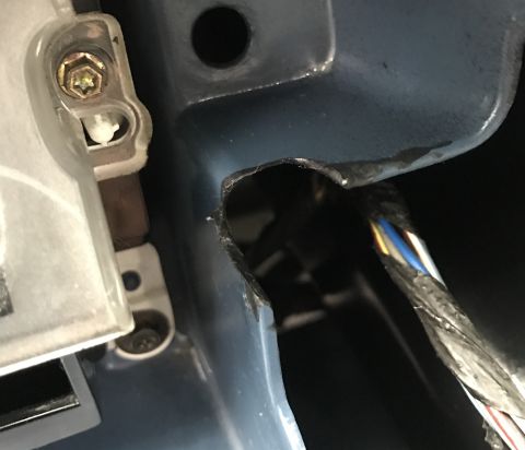 1995 Ford Bronco - A close-up view shows a damaged blue metal panel with a hole cut into it, revealing wires and a dark interior. A clear plastic component wi…