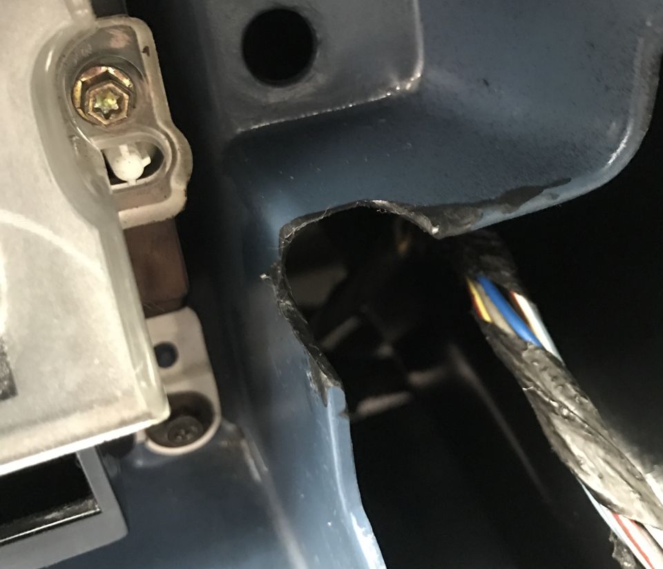 Damaged blue metal panel with a hole and wires, and a clear plastic component with a screw.