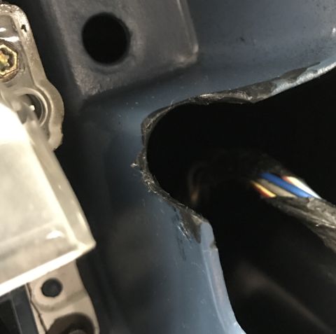 1995 Ford Bronco - A close-up view shows a damaged opening in a blue vehicle's body panel, revealing a bundle of wires passing through. A clear plastic compon…