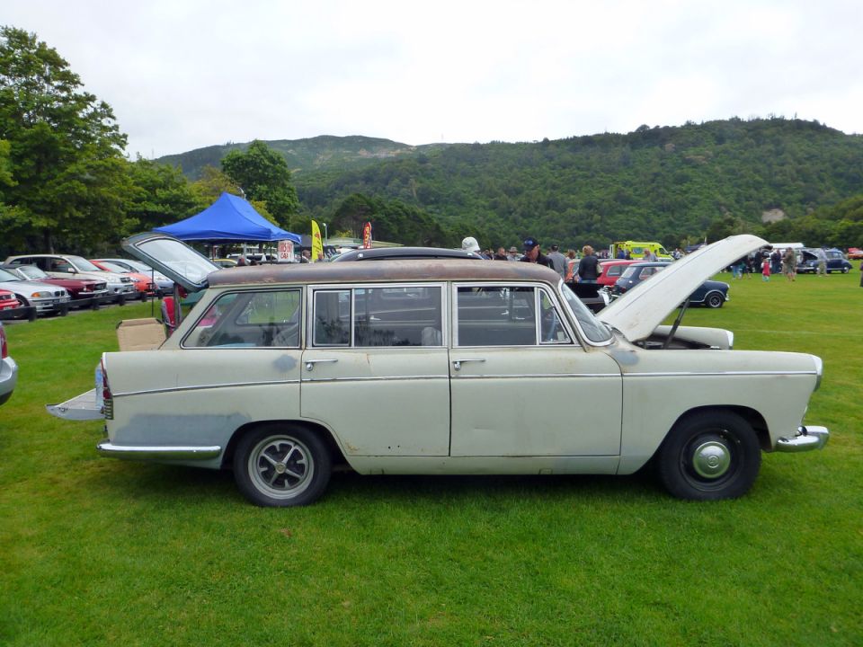Light-colored station wagon with open hood and hatch, parked on grass at an outdoor event.