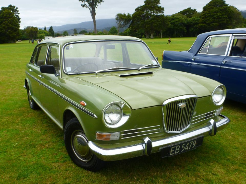Light green vintage sedan with chrome accents parked on grass, blue car behind it.