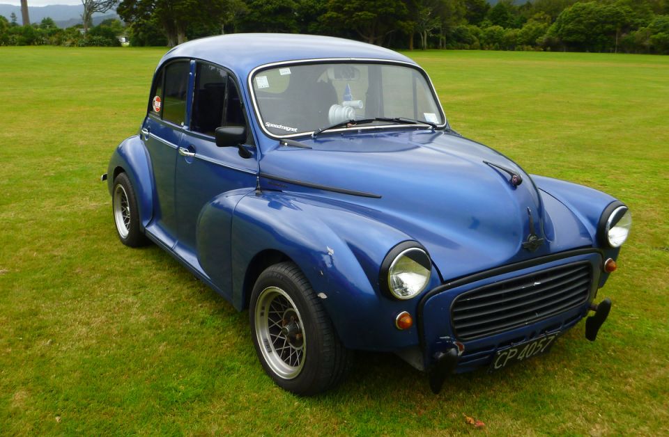 Blue classic car parked on grass, front 3/4 view.