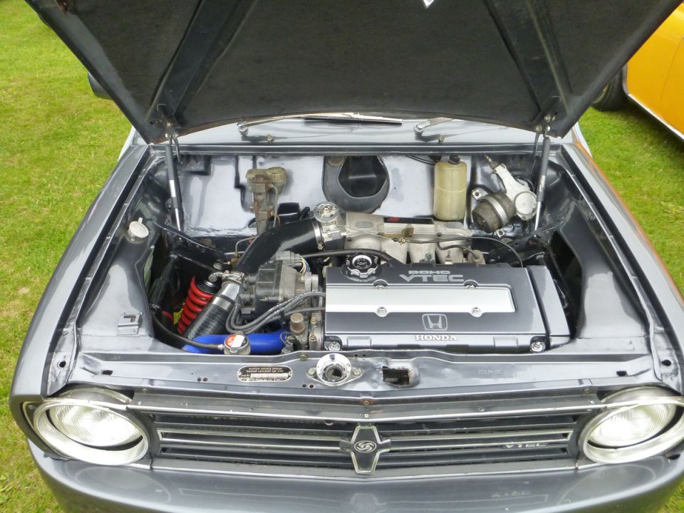 Gray car engine bay with Honda DOHC VTEC engine, intake piping, and red coilover spring.