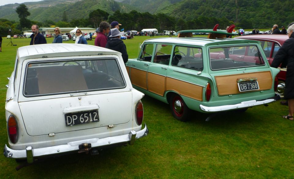 Two vintage station wagons, one white and one green with wood paneling, parked on a grassy field.