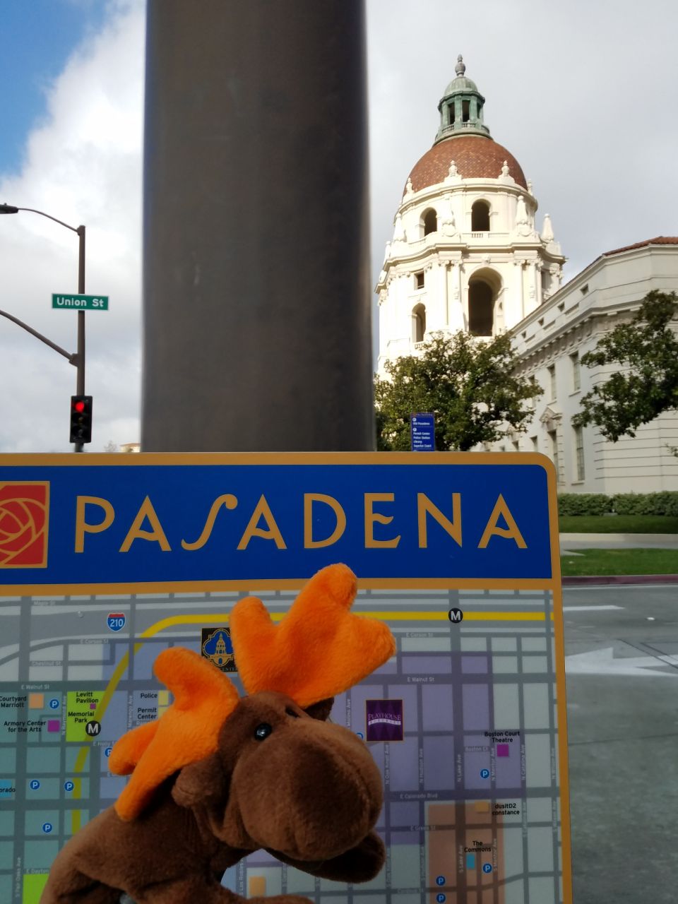 Plush moose toy in front of a Pasadena map with city hall in the background.