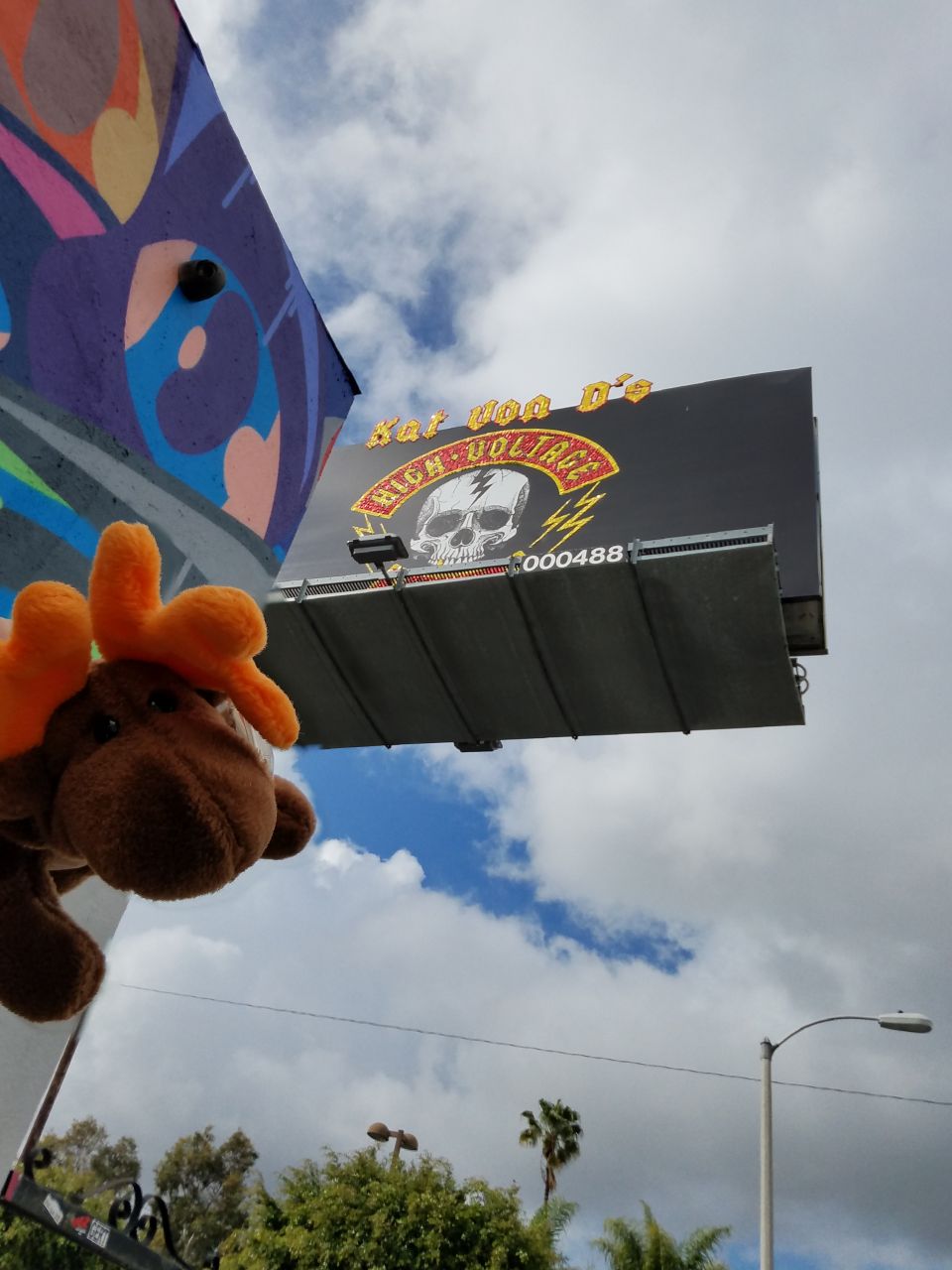 Plush toy moose in front of a billboard with a skull graphic and text "Hot Rod D's High Voltage".