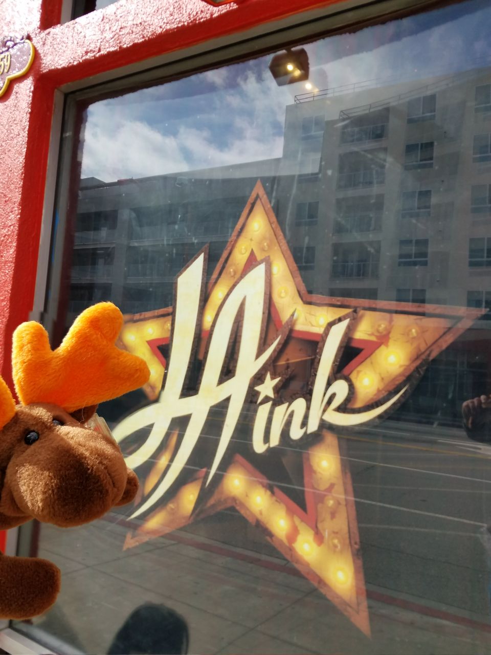 Stuffed moose in front of a window with a large illuminated star sign that says "Hink".