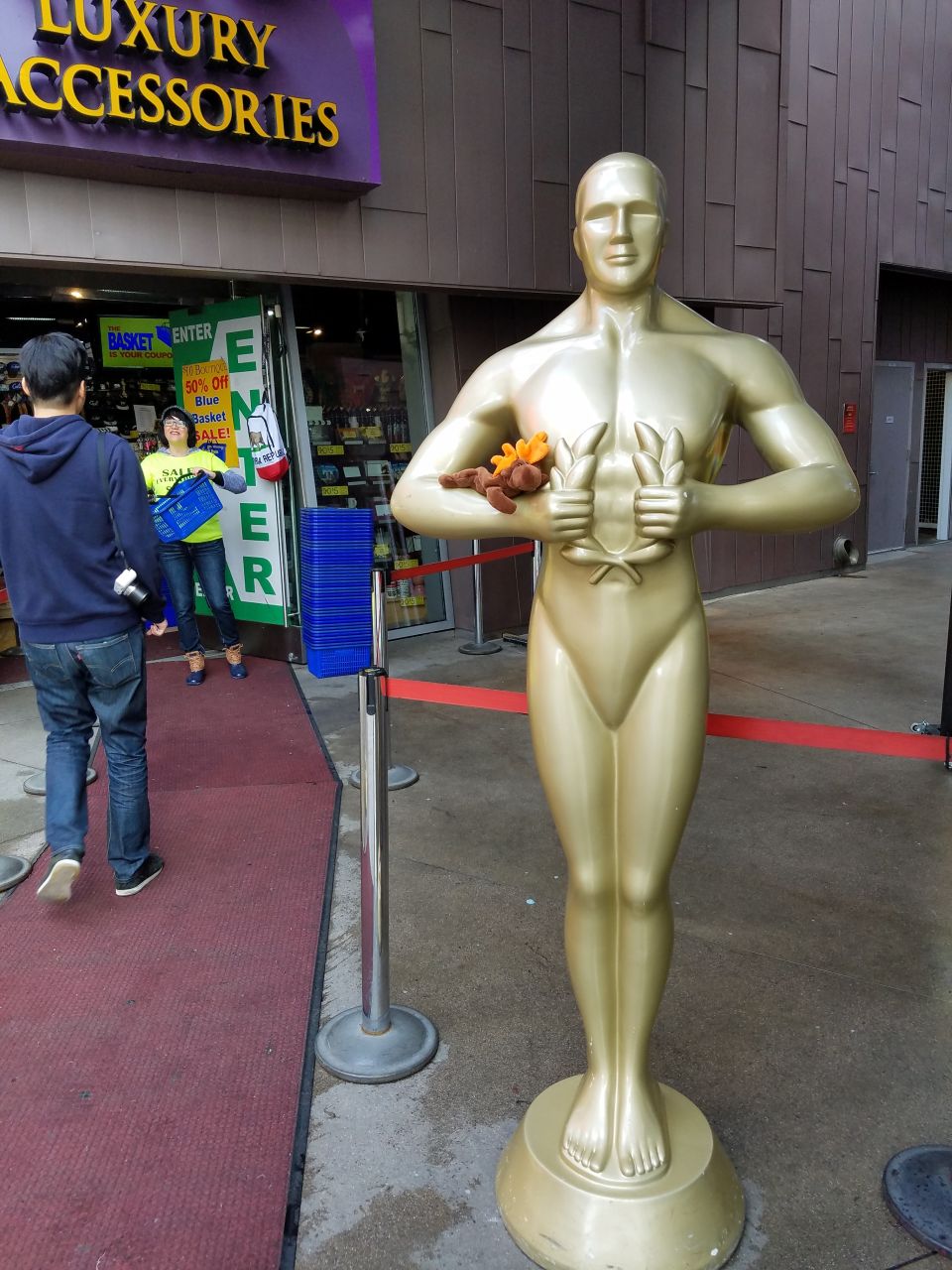 Golden Oscar statue outside a store with people entering and exiting.