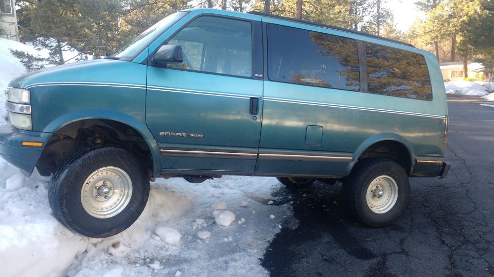 Teal green 1995 GMC Safari van with lifted suspension and off-road tires in the snow.